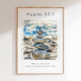 Psalm 37:7 - Christian art print with watercolour stacked pebbles and soft blue bokeh background and Rest In The Lord scripture verse.